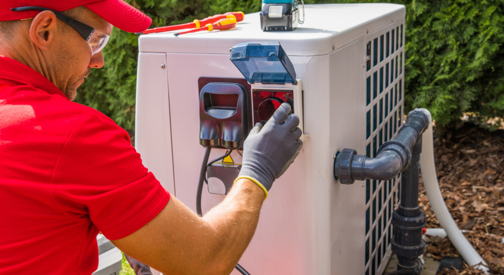 Technician in red uniform and safety glasses servicing an outdoor pool heat pump unit