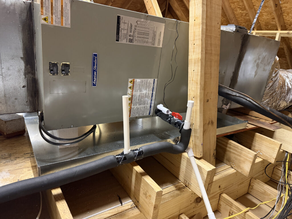 American Standard air handler unit installed in an attic with PVC condensate drain lines and insulated refrigerant lines